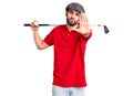 Young handsome man with beard playing golf holding club and ball with open hand doing stop sign with serious and confident Royalty Free Stock Photo