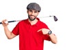 Young handsome man with beard playing golf holding club and ball pointing finger to one self smiling happy and proud Royalty Free Stock Photo