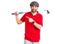 Young handsome man with beard playing golf holding club and ball smiling happy pointing with hand and finger Royalty Free Stock Photo