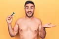 Young handsome man with beard shirtless holding depilation razor over yellow background celebrating achievement with happy smile