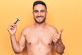 Young handsome man with beard shirtless holding depilation razor over yellow background smiling happy and positive, thumb up doing Royalty Free Stock Photo