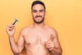 Young handsome man with beard shirtless holding depilation razor over yellow background smiling with an idea or question pointing Royalty Free Stock Photo