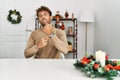 Young handsome man with beard sitting on the table by christmas decoration in hurry pointing to watch time, impatience, looking at Royalty Free Stock Photo