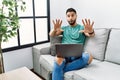 Young handsome man with beard using computer laptop sitting on the sofa at home afraid and terrified with fear expression stop Royalty Free Stock Photo