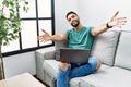 Young handsome man with beard using computer laptop sitting on the sofa at home looking at the camera smiling with open arms for Royalty Free Stock Photo