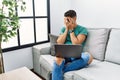 Young handsome man with beard using computer laptop sitting on the sofa at home with sad expression covering face with hands while Royalty Free Stock Photo