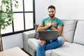 Young handsome man with beard using computer laptop sitting on the sofa at home smiling with hands on chest with closed eyes and Royalty Free Stock Photo