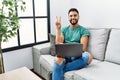 Young handsome man with beard using computer laptop sitting on the sofa at home smiling with happy face winking at the camera Royalty Free Stock Photo