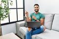 Young handsome man with beard using computer laptop sitting on the sofa at home smiling and looking at the camera pointing with Royalty Free Stock Photo