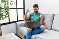 Young handsome man with beard using computer laptop sitting on the sofa at home very happy and excited doing winner gesture with Royalty Free Stock Photo