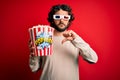 Young handsome man with beard watching movie holding popcorns over red background with angry face, negative sign showing dislike Royalty Free Stock Photo