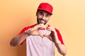Young handsome man with beard wearing baseball cap and t-shirt smiling in love doing heart symbol shape with hands