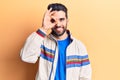 Young handsome man with beard wearing casual jacket doing ok gesture with hand smiling, eye looking through fingers with happy Royalty Free Stock Photo