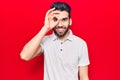 Young handsome man with beard wearing casual polo doing ok gesture with hand smiling, eye looking through fingers with happy face Royalty Free Stock Photo
