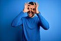 Young handsome man with beard wearing casual sweater and glasses over blue background doing ok gesture like binoculars sticking Royalty Free Stock Photo