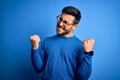 Young handsome man with beard wearing casual sweater and glasses over blue background very happy and excited doing winner gesture Royalty Free Stock Photo