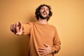 Young handsome man with beard wearing casual sweater standing over yellow background laughing at you, pointing finger to the Royalty Free Stock Photo