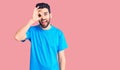 Young handsome man with beard wearing casual t-shirt doing ok gesture with hand smiling, eye looking through fingers with happy Royalty Free Stock Photo