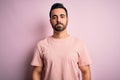 Young handsome man with beard wearing casual t-shirt standing over pink background with serious expression on face Royalty Free Stock Photo