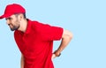 Young handsome man with beard wearing delivery uniform suffering of backache, touching back with hand, muscular pain Royalty Free Stock Photo