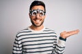 Young handsome man with beard wearing optometry glasses over isolated white background smiling cheerful presenting and pointing Royalty Free Stock Photo