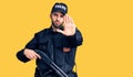 Young handsome man with beard wearing police uniform holding shotgun with open hand doing stop sign with serious and confident Royalty Free Stock Photo