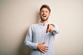 Young handsome man with beard wearing striped shirt standing over white background laughing at you, pointing finger to the camera Royalty Free Stock Photo