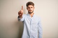 Young handsome man with beard wearing striped shirt standing over white background Pointing with finger up and angry expression, Royalty Free Stock Photo