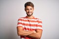 Young handsome man with beard wearing striped t-shirt standing over white background happy face smiling with crossed arms looking Royalty Free Stock Photo