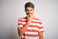 Young handsome man with beard wearing striped t-shirt standing over white background looking confident at the camera smiling with Royalty Free Stock Photo