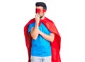 Young handsome man with beard wearing super hero costume looking stressed and nervous with hands on mouth biting nails