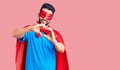 Young handsome man with beard wearing super hero costume smiling in love doing heart symbol shape with hands