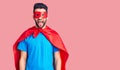 Young handsome man with beard wearing super hero costume sticking tongue out happy with funny expression