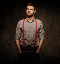 Young handsome man with beard wearing suspenders and posing on dark background.