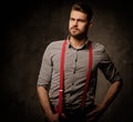 Young handsome man with beard wearing suspenders and posing on dark background. Royalty Free Stock Photo