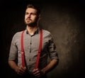 Young handsome man with beard wearing suspenders and posing on dark background. Royalty Free Stock Photo