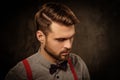 Young handsome man with beard wearing suspenders and posing on dark background. Royalty Free Stock Photo