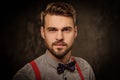 Young handsome man with beard wearing suspenders and posing on dark background. Royalty Free Stock Photo