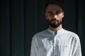 Young handsome man with beard and in white shirt is standing against dark green background Royalty Free Stock Photo