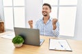 Young handsome man with beard working at the office using computer laptop very happy and excited doing winner gesture with arms Royalty Free Stock Photo