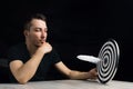 Man sits at table holding dart board with quill pen stuck in the center of the target on black background Royalty Free Stock Photo
