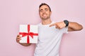 Young handsome man with blue eyes holding birthday present over isolated pink background very happy pointing with hand and finger Royalty Free Stock Photo