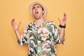 Young handsome man with blue eyes on vacation wearing summer florar shirt and hat crazy and mad shouting and yelling with Royalty Free Stock Photo