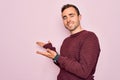 Young handsome man with blue eyes wearing casual sweater standing over pink background Inviting to enter smiling natural with open Royalty Free Stock Photo