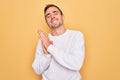 Young handsome man with blue eyes wearing casual sweater standing over yellow background clapping and applauding happy and joyful, Royalty Free Stock Photo