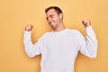 Young handsome man with blue eyes wearing casual sweater standing over yellow background very happy and excited doing winner Royalty Free Stock Photo
