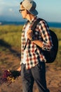 Young handsome man, in a cap and glasses, with a backpack, traveling and walking in nature, a man with a bouquet of wildflowers Royalty Free Stock Photo