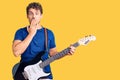 Young handsome man with curly hair playing electric guitar covering mouth with hand, shocked and afraid for mistake Royalty Free Stock Photo