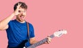 Young handsome man with curly hair playing electric guitar smiling happy doing ok sign with hand on eye looking through fingers Royalty Free Stock Photo