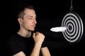 Man and dart board with a quill pen stuck in the center of the target on a black background in a low key Royalty Free Stock Photo